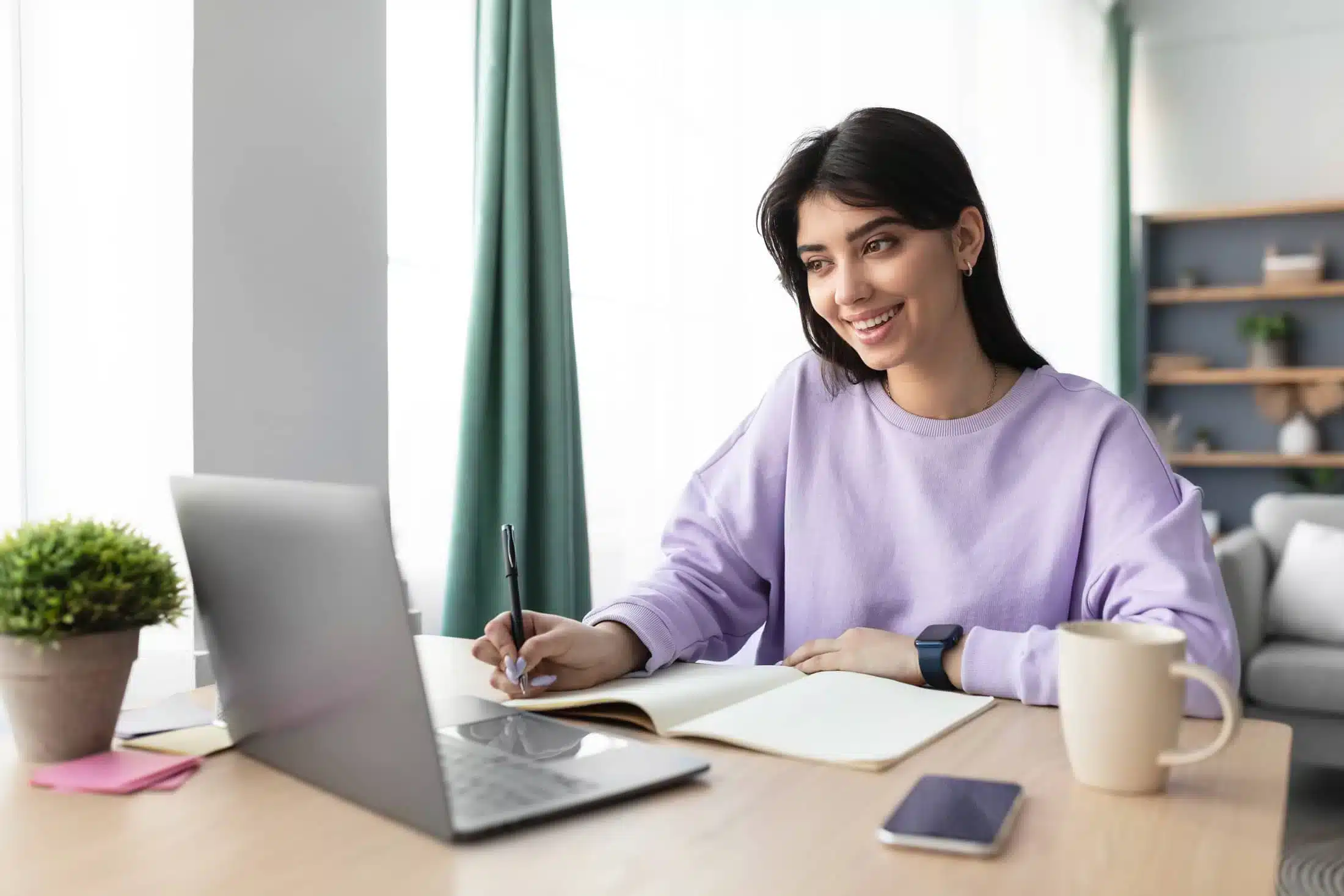 Student sits in front of a laptop and writes in a notepad