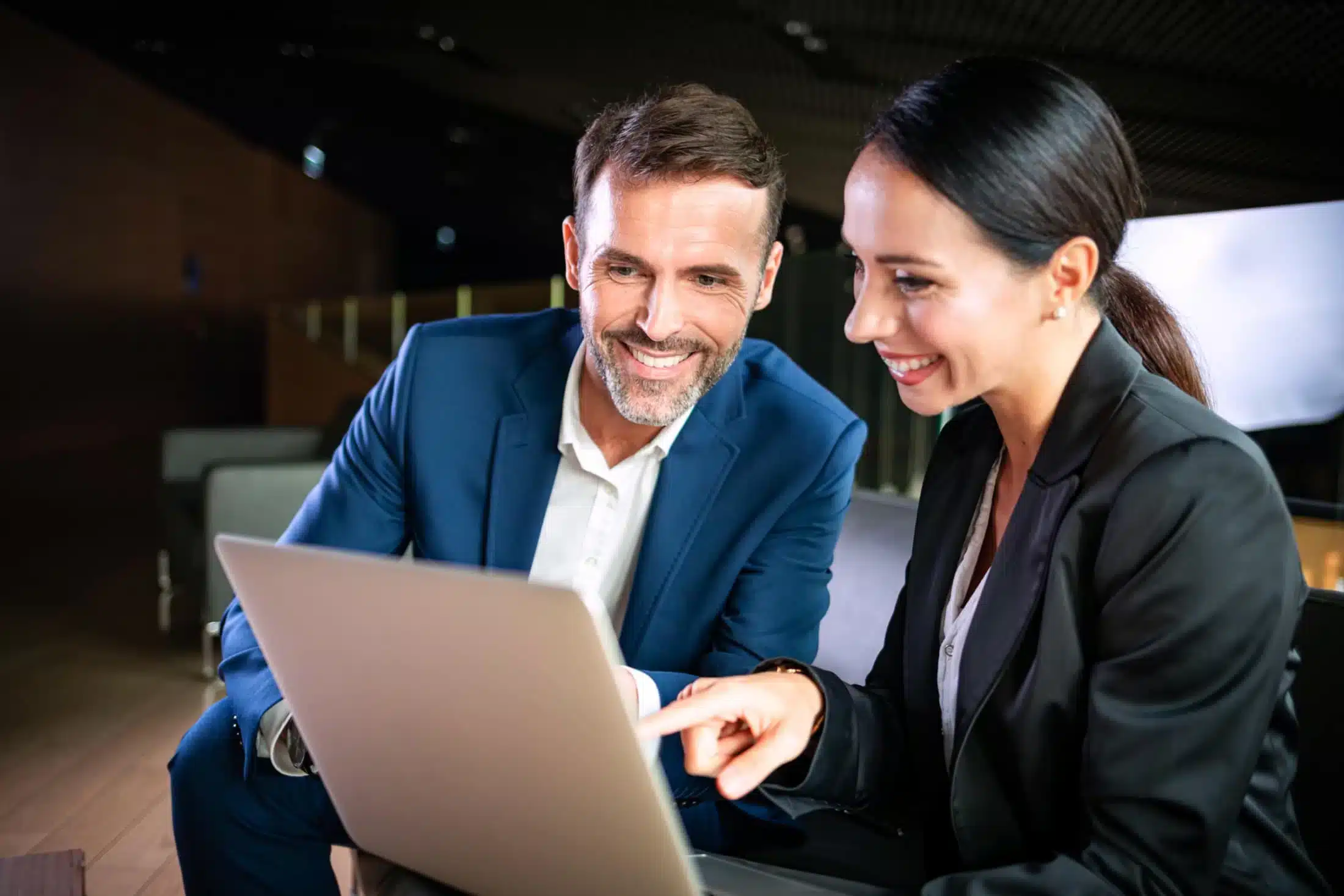 Two happy people sit in front of a work laptop and discuss