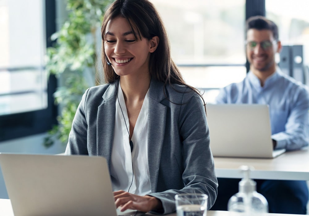 Happy people sitting in an office in front of a laptop and talking on the phone